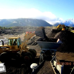 Using an excavator to break up large piles of asphalt millings to be processed through the pug mill and paved shortly after